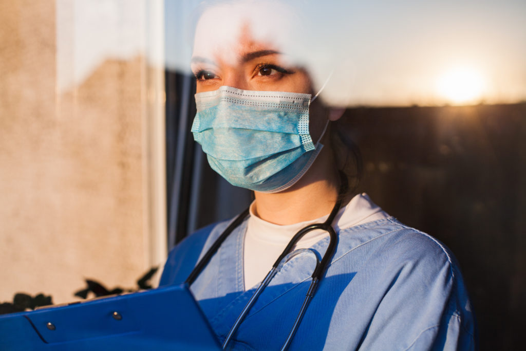 A young female medical professional wearing ppe gazes out a window.