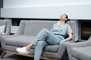 A woman wearing scrubs rests on a couch