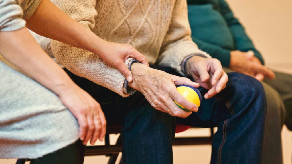 An elderly man squeezes a ball with an aide.