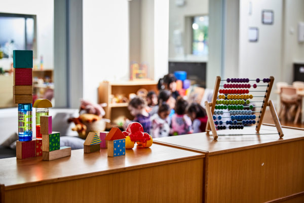 Interior photography of toys in a childcare center with preschoolers out of focus in the background.