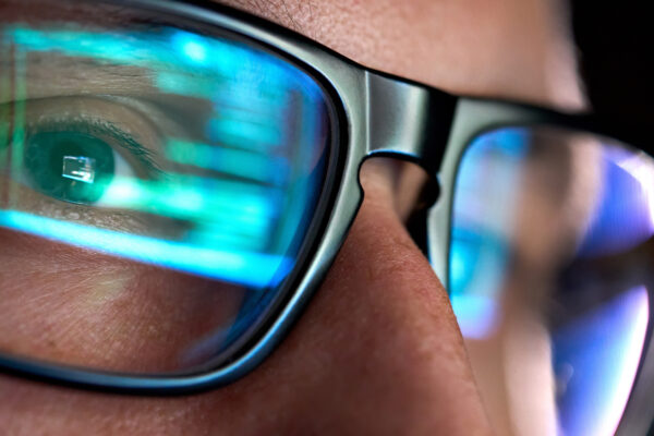 An IT worker wearing glasses is focused on code data, denoting hospital cyberattack risk.