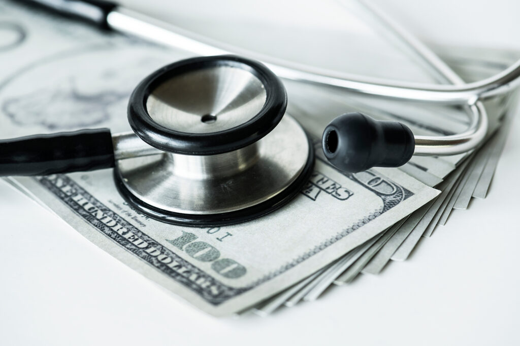 A closeup of cash and a stethoscope, expressing the concept of healthcare and hospital costs.