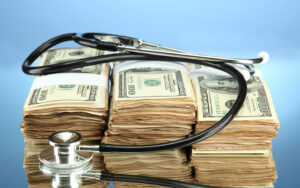 A stethoscope sits on top of a stack of dollars, showing the concept of healthcare financials 2024.