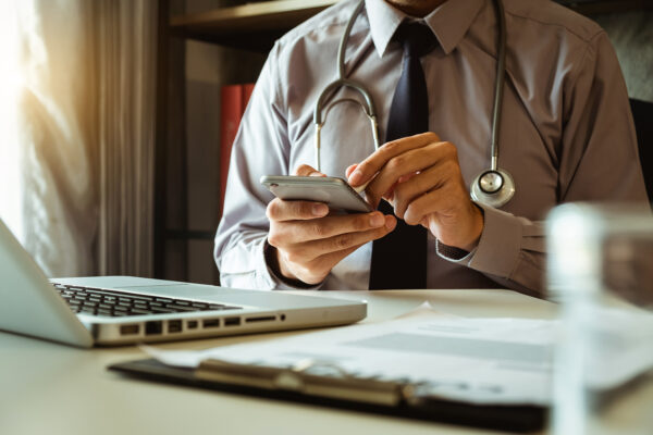 A close up of a male doctor typing on a mobile phone, representing concierge physician care.