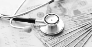A stethoscope sits on money and a financial statement, representing private equity healthcare slowdown.