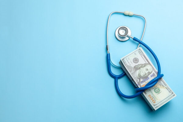 A stethoscope wraps around a stack of cash, representing the tension between Medicare Advantage plans and hospitals.